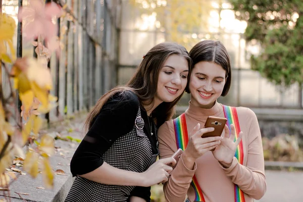 Zwei schöne Studentinnen beim Telefonieren im Herbstpark — Stockfoto