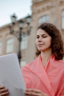 Üniversitenin yanında duran kadının elinde menkul kıymetler var.