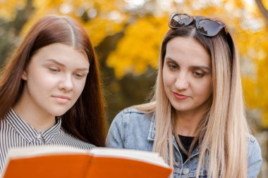 İki kız, zevkle, sonbahar parkında bir kitap okudular.