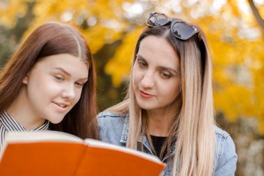 İki güzel genç kız, zevkle, sonbahar parkında bir kitap okumak