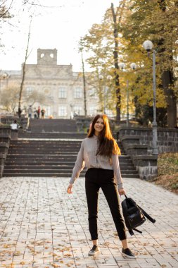 Sırt çantası olan kız üniversiteye giden merdivenlerin yanında duruyor.