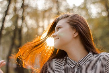 Gün batımı güneş ışığı saçında parıldayan kahverengi saçlı bir kızın portresi