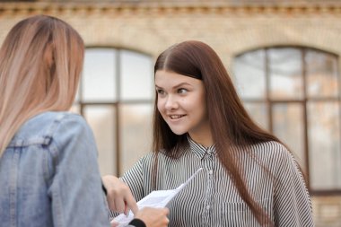 Mutlu kız üniversitenin yanında duruyor ve kağıt ile yetişkin bakmak
