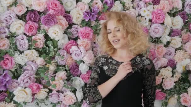 Blonde zingt in de buurt van een muur van bloemen — Stockvideo