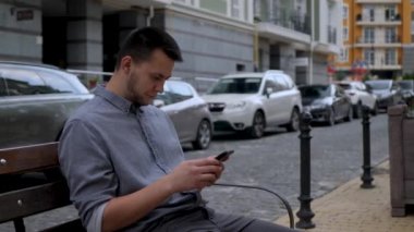 Adam dışarıda otururken akıllı telefon kullanıyor.