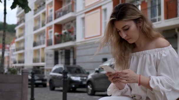 Nettes Mädchen verwenden weißes Smartphone im Freien — Stockvideo