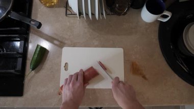 İşlevsel bir mutfakta, deneyimli bir erkek eli kesme tahtasındaki malzemeleri keser. Pişirme süreci: sosis kesme