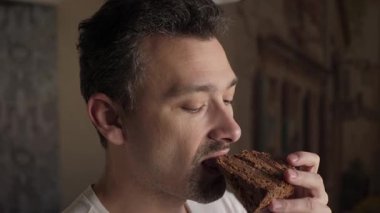 Adam bir dilim zengin çikolatalı pastanın tadını çıkarıyor. Zevk ve hoşgörü sergiliyor. Bu an, yemek, tatlı ve yaşam tarzı temaları için mükemmel bir zevk ve tatmini vurguluyor.