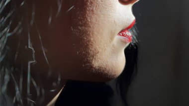 Kadın yüzünün alt kısmı kırmızı dudaklı koyu renk arka planda düşük tuşlu modda.
