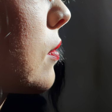 Kadın yüzünün alt kısmı kırmızı dudaklı koyu renk arka planda düşük tuşlu modda.