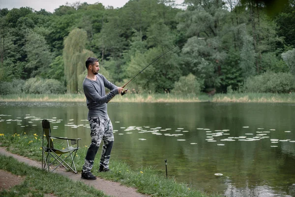 Fisherman cast fishing rod in lake or river water. Man with spinning tackle in green forest. Adventure, sport, activity. Spin fishing, angling, catching. Healthy lifestyle.