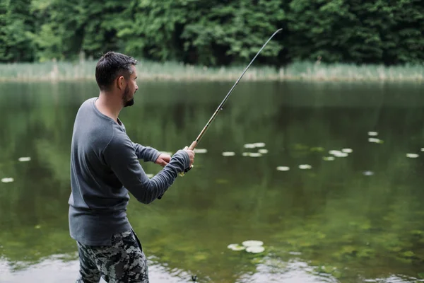 Fisherman cast fishing rod in lake or river water. Man with spinning tackle in green forest. Adventure, sport, activity. Spin fishing, angling, catching. Healthy lifestyle.