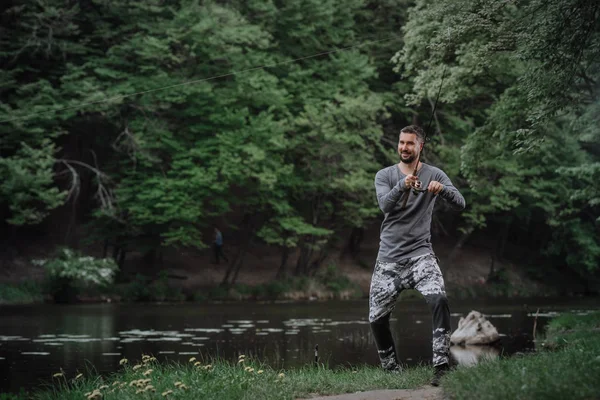 Fisherman cast fishing rod in lake or river water. Man with spinning tackle in green forest. Adventure, sport, activity. Spin fishing, angling, catching. Healthy lifestyle.