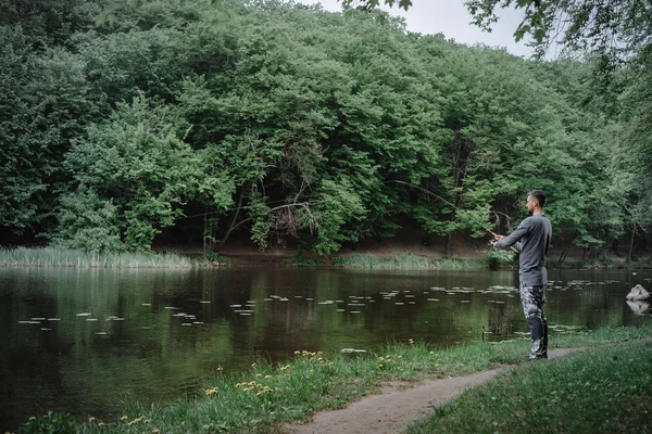 Fisherman cast fishing rod in lake or river water. Man with spinning tackle in green forest. Adventure, sport, activity. Spin fishing, angling, catching. Healthy lifestyle.