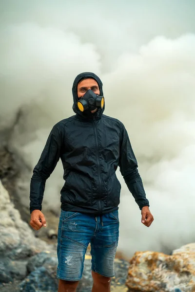 A man in a respirator in the very center of a volcano crater. Sulfur puffs of toxic smoke are hazardous to health. Concept: adventure, danger, defense, tourism.