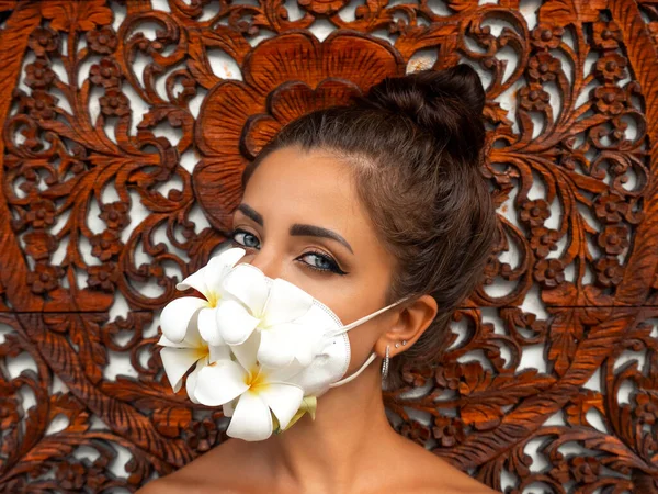 Girl in an antiviral mask on an unusual background. Fashion photo. Pandemic, virus, coronavirus, masked girl spring has come. Spring fashion, model in a mask of flowers