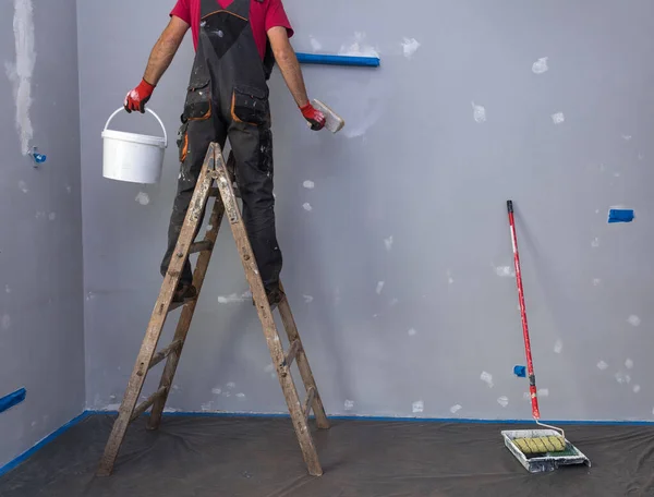 Casa Pintor, pintor homem no trabalho, com escada de madeira e parede em branco — Fotografia de Stock