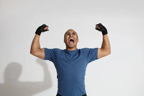 Strength, energy, power, sports and determination concept. Picture of determined young dark skinned sportsman roaring in studio, pumping fists and keeping mouth wide opened, showing his muscles