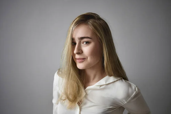 People and lifestyle concept. Beautiful young female manager with straight fair hair and green eyes posing in white blouse at office, having joyful happy look, rejoicing at career achievements