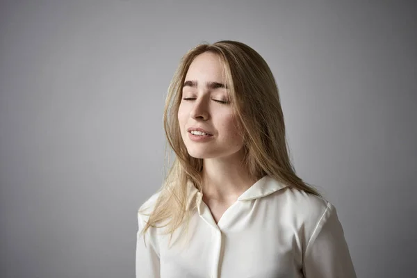 Human facial expressions, emotions and reaction. Portrait of elegant beautiful young European female in white shirt closing eyes as if listening to good pleasant music or dreaming, posing indoors