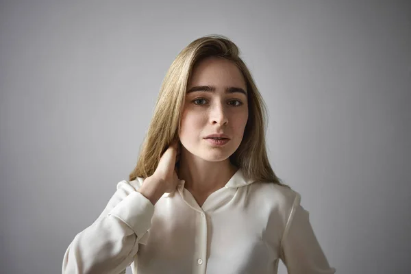 Stylish young businesswoman wearing formal white blouse touching her neck and looking at camera having serious or confused kook. People, fashion, style, beauty and human facial expressions