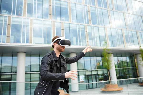 Futuristic technology, innovation, entertainment and gaming concept. Bearded young Caucasian man using virtual reality oculus rift headset on street, gesturing as if touching something in the air