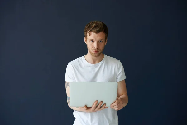Always in touch. Portrait of attractive confident young European freelancer dressed in casual clothes holding laptop computer while working remotely, using wireless high-speed internet connection