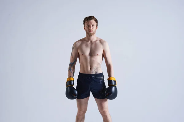 Cropped portrait of self-determined young kickboxer standing shirtless in gym, having serious confident look, ready for workout. People, determination, fitness, sports and martial arts concept
