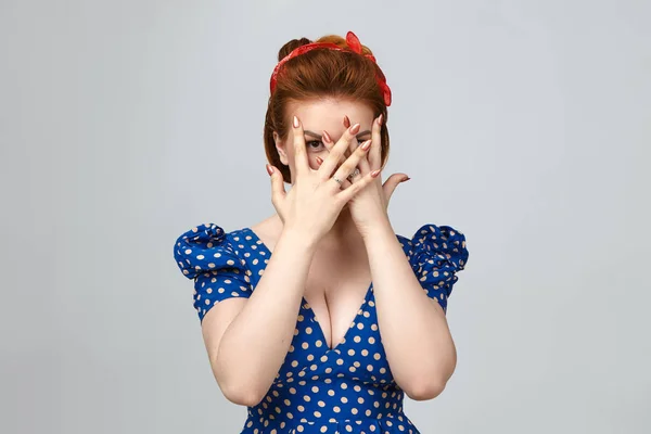 Scared afraid young lady dressed in stylish vintage clothes covering face with both hands, peeping at camera through fingers.