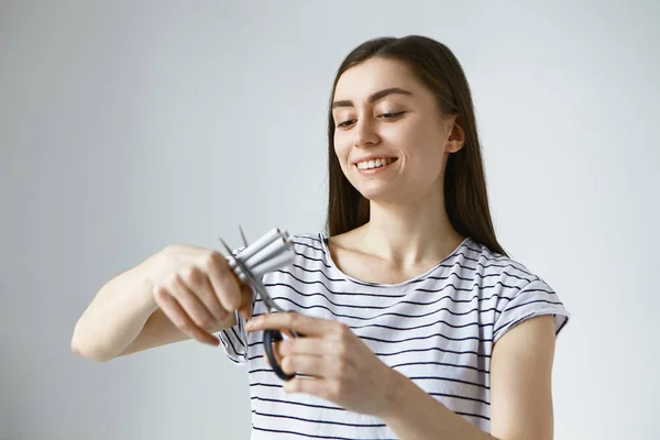 Happy young European woman feeling free of destructive unhealthy tobacco addiction, holding cigarettes, cutting them in halves using scissors, smiling joyfully.