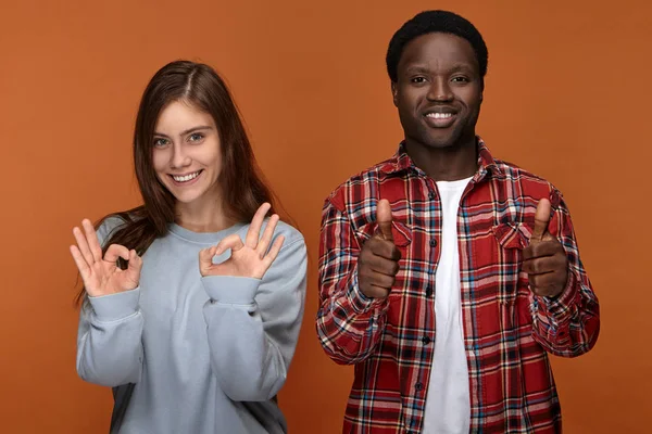 Good job. Well done. Happy positive young caucasian woman making ok gesture and handsome joyful afro american man showing thumbs up