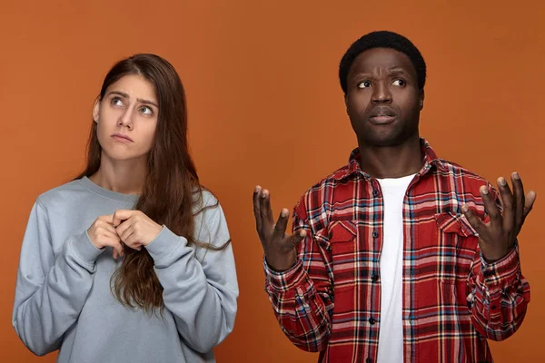Frustrated black dark-skinned guy shrugging shoulders and frowning with upset white girlfriend having periods
