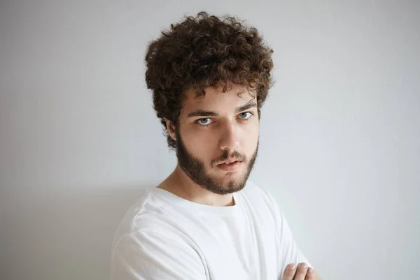 Gloomy young man with fuzzy thick beard staring at camera with displeased look
