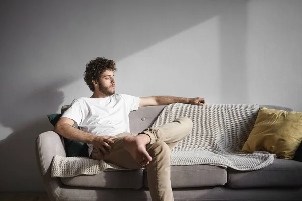 Man with thick beard relaxing indoors, sitting on cozy couch in living room.