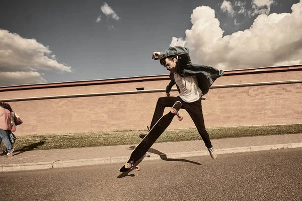 Professional young caucasian male skateboarder practicing skills outside. Handsome teenager in black jeans jumping while trying to do complex trick using long board on street