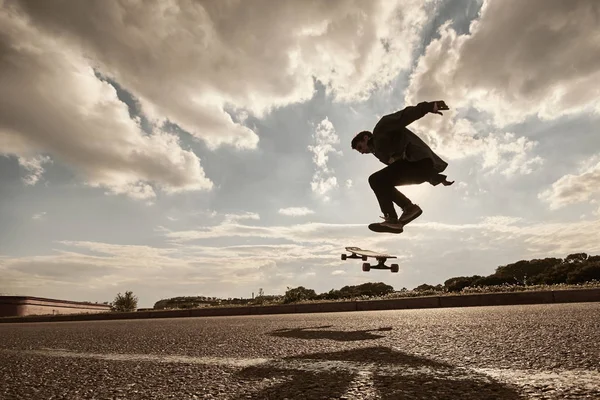 Youth, leisure, recreation, hobby, active lifestyle and extreme sports. Outdoor portrait of silhouette of teenager jumping high with skate in air going to land on board while doing kick flip