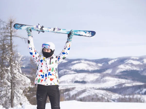 girl holding skis in her hands Happy girl holding skis and ski poles in hands, sitting in snow