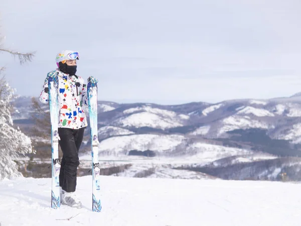 girl holding skis in her hands Happy girl holding skis and ski poles in hands, sitting in snow