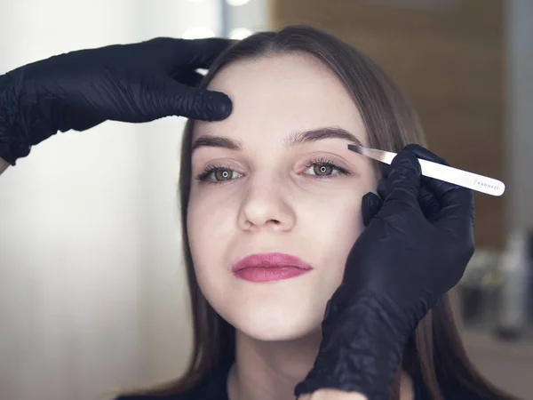 Artistic design of eyebrows. Correction. Pin forceps Woman having her eye brows tinted. Semi-permanent makeup for eyebrows. Focus on model\'s face and eyebrow