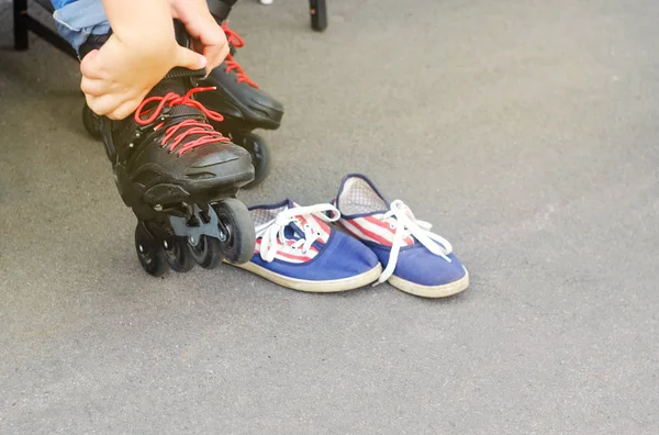 the child in shod black rollers with red laces and blue moccasins for dressing up shoes on a skating rink where people go for a drive, a theme of sports and recreation