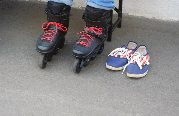 the child in shod black rollers with red laces and blue moccasins for dressing up shoes on a skating rink where people go for a drive, a theme of sports and recreation