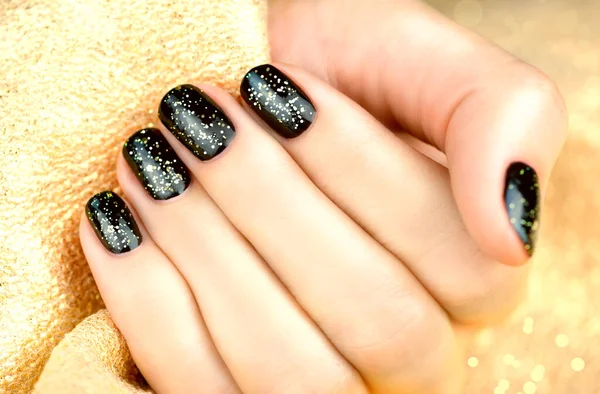 Female hand with black manicure and gold sparkles on a golden background