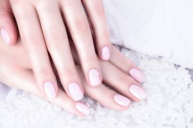 Çıplak tırnak cilası. Beyaz arka planda incileri olan bej renkli hassas manikür..