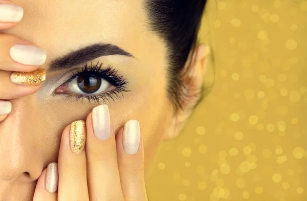 Female face with white and gold makeup and gold manicure on a gold background. Close up