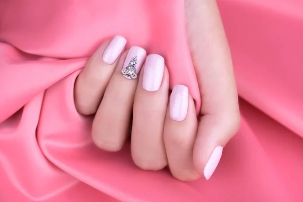 Women\'s fingers with soft pink manicure and rhinestones on the nails. Pink background. Close-up.