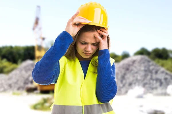 Young female engineer or architect suffering headache because of stressful job as exhausted employee concept on construction site background
