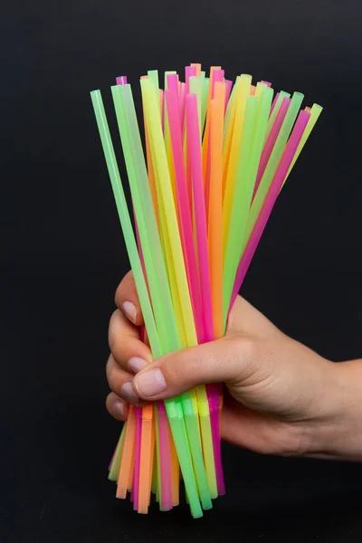 Ecological single use plastic issue concept with hand holding bunch of colorful drink straws isolated on black background