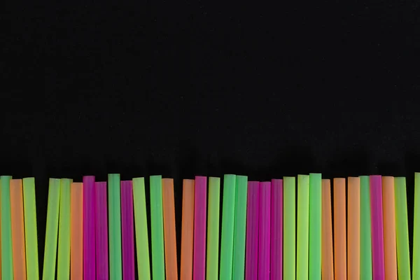 Lined up bright colored drink straws pattern art design as nature issue of disposable single use plastic product concept isolated on black background