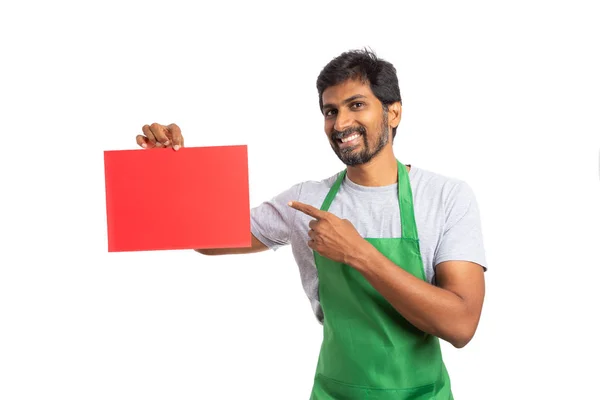 Enthusiastic indian shop manager or employee presenting with index finger blank copyspace for advertising on red paper isolated on white