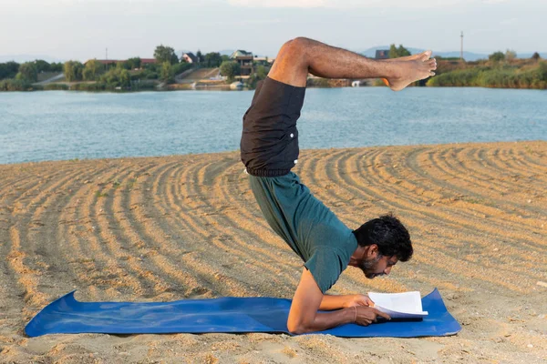 印度瑜伽大师阅读一本书在倒立的位置与自然背景在海滩 — 图库照片